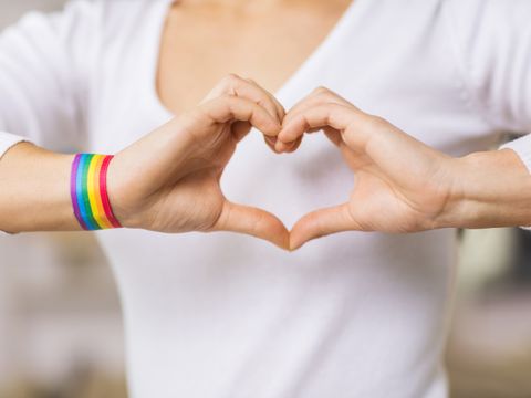 Frau mit Armband in Regenbogenfarben bildet ein Herz mit den Händen
