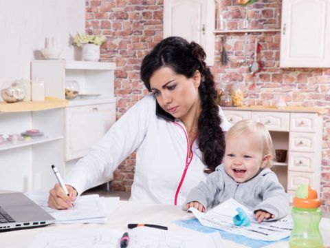 Mutter mit Kleinkind am Schreibtisch bei der Arbeit zu Hause