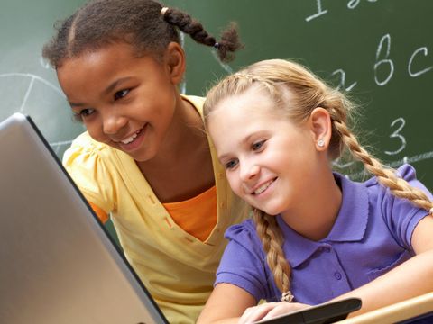zwei Kinder vor einem Laptop mit Tafel im Hintergrund
