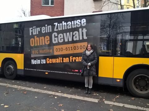 Bildvergrößerung: Frauen- und Gleichstellungsbeauftragte Annukka Ahonen vor einem BVG-Bus mit dem Schriftzug der Kampagne gegen häusliche Gewalt
