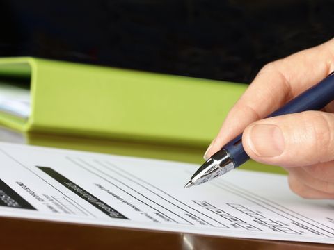 Hand füllt mit Kugelschreiber Formular aus, im Hintergrund ein grüner Ordner