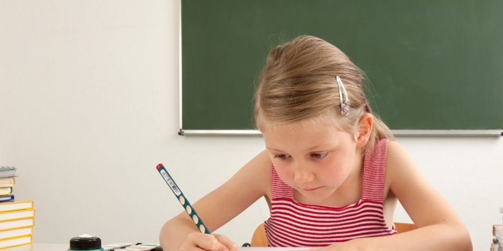 Mädchen sitzt im Unterricht und schreibt mit Bleistift 