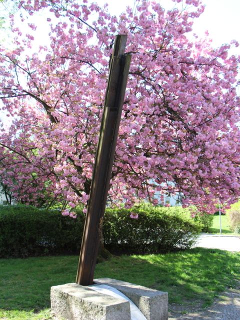 Bildvergrößerung: Mahnmal mit einer rosa Blütenpracht im Hintergrund
