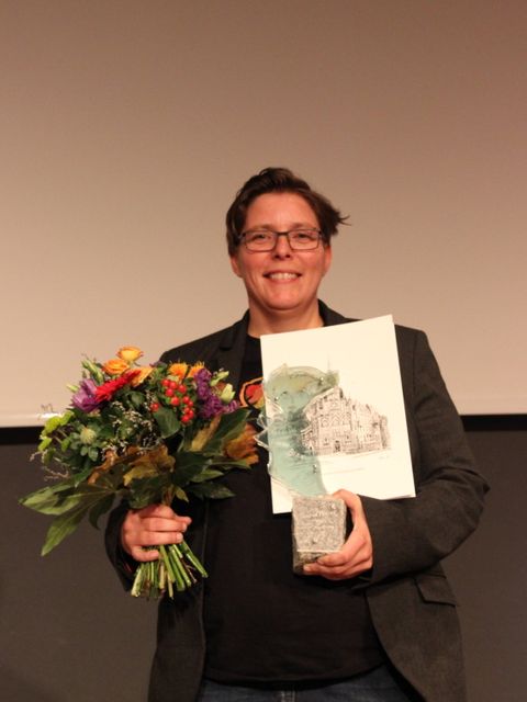 Bildvergrößerung: Frauenpreisträgerin 2021 Claudia Engelmann. Sie hält einen Blumenstrauß und die Frauenpreis-Trophäe in den Händen. 