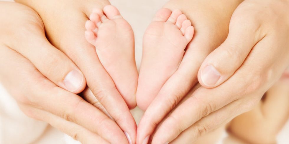 Die Füße eines Neugeborenen werden von den Händen der Eltern umrahmt. Die Hände bilden ein Herz.