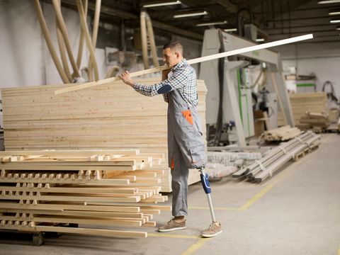 Behinderter junger Mann mit künstlichem Bein arbeitet in der Möbelfabrik