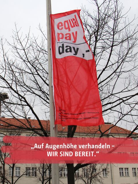 Bildvergrößerung: Rote Fahne mit der Aufschrift Equal Pay day und Schriftzug im Vordergrund mir dem diesjährigen Motto