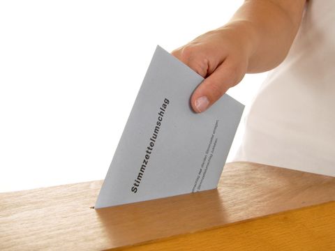 Stimmzettel wird in Wahlurne gesteckt