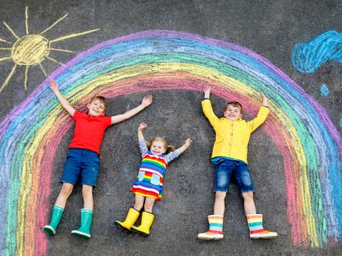 Kinder mit Malerei eines Regenbogens auf der Straße liegend