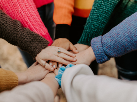 Nahaufnahme von aufeinander gestapelten Händen als Zeichen für Zusammenhalt und Teamwork.