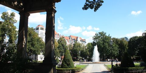 Zu sehen ist eine Ansicht des Viktoria-Luise-Platzes von den Kolonnaden aus. In der Mitte der Springbrunnen mit Fontäne