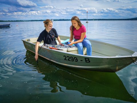 Zwei Mädchen sitzen im Boot und nehmen eine Wasserprobe