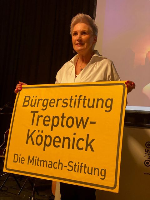 Die Vorsitzende des Stiftungsrates Annett Maurer würdigt die Stiftung und motiviert zum „Mitmachen mit einem Schild auf dem steht: Bürgerstiftung Treptow-Köpenick - Die Mitmach-Stiftung