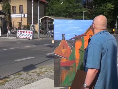 ein Mann malt am Straßenrand ein Gebäude auf eine Leinwand
