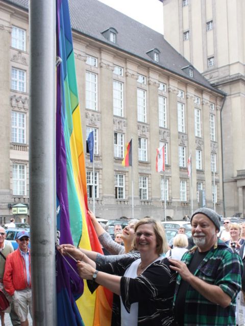 Bildvergrößerung: Bezirksbürgermeisterin Angelika Schöttler hisst gemeinsam mit dem Sprecher des Regenbogenfonds e.V., Gerhard Hoffmann, die Regenbogenfahne vor dem Rathaus Schöneberg