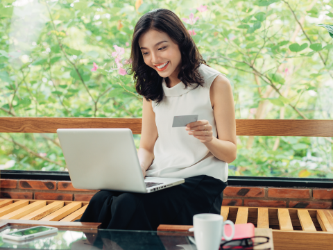 Junge Frau in einem Café mit ihrem Laptop auf dem Schoß und ihrer Kreditkarte in der Hand