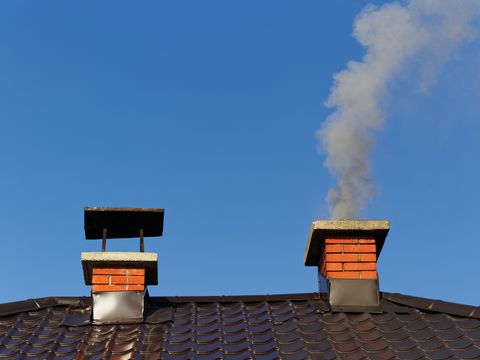 Rauch aus gemauertem Schornstein auf Dach gegen blauen Himmel