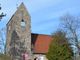 Dorfkirche Alt-Buckow Gesamtansicht von der Straße: schlichte Kirche mit Sichtmauerwerk, eckigem Kirchturm und Satteldach-Kirchenschiff, eingemauert mit Bäumen und Büschen im Vordergrund