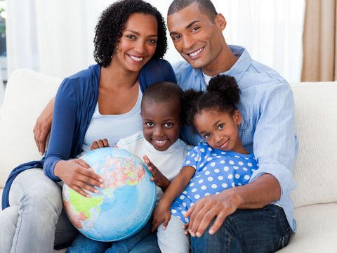 Familie mit 2 kleinen Kindern sitzt mit einem Globus auf dem Sofa
