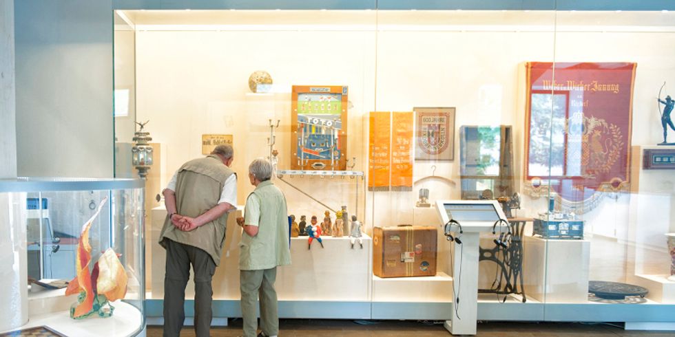 Zwei Besucher in der Ausstellung 99 x Neukölln betrachten Objekte in Vitrinen