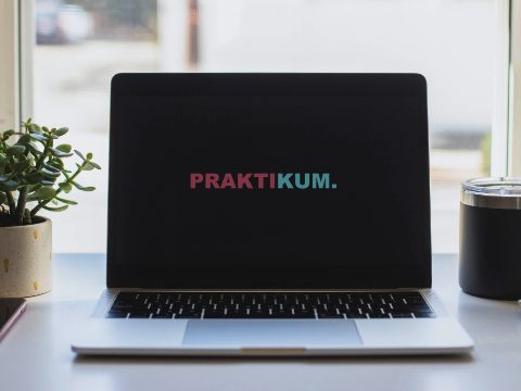 Laptop mit Schriftzug Praktikum, Tasse, Pflanze, Smartphone auf dem Schreibtisch