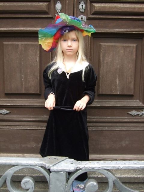 Bildvergrößerung: Ein Mädchen ist mit einem Samtkleid und einem bunten Hut auf verkleidet.