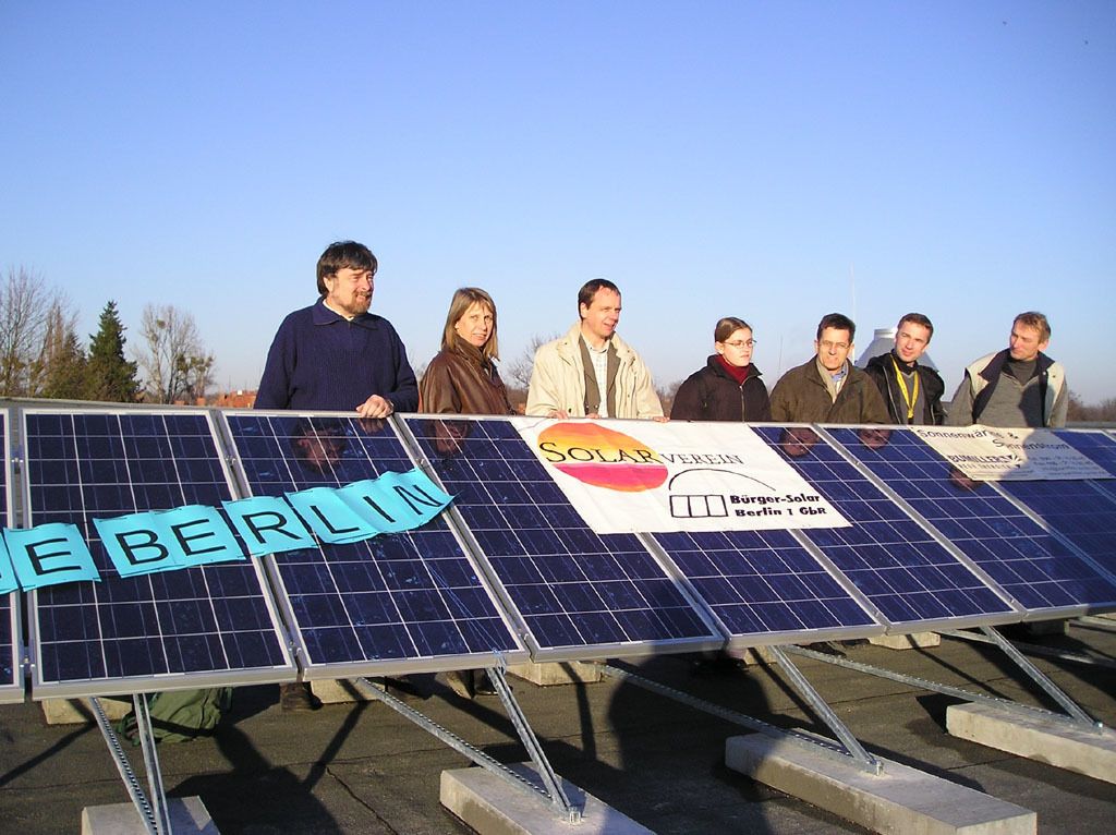 Hinter einer Reihe von Fotovoltaikmodulen stehen sieben Menschen.