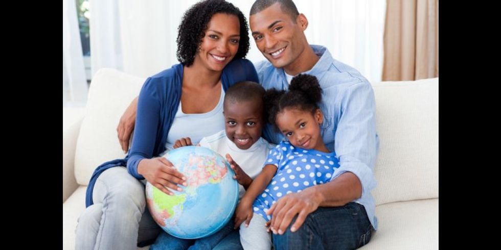 Familie mit 2 kleinen Kindern sitzt mit einem Globus auf dem Sofa