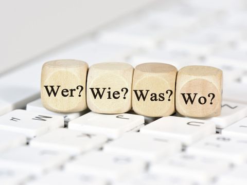 Auf einer Tastatur liegen vier Würfel mit den Aufschriften 'Wer?', 'Wie?', 'Was?', 'Wo?'