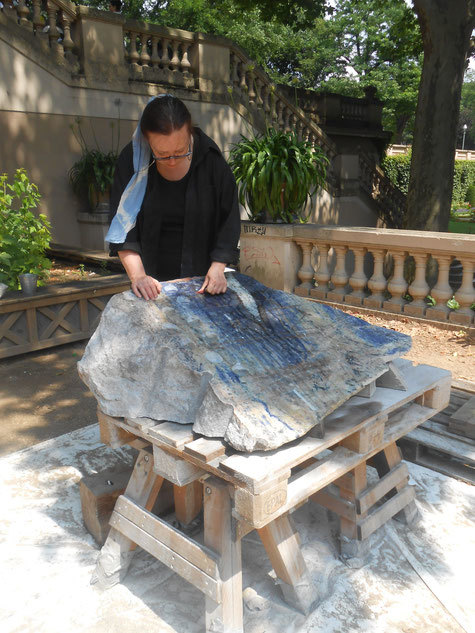 Die Bildhauerin Silvia Fohrer berührt mit beiden Händen einen großen blauen Stein. Im Hintergrund eine Treppe des Körnerparks.