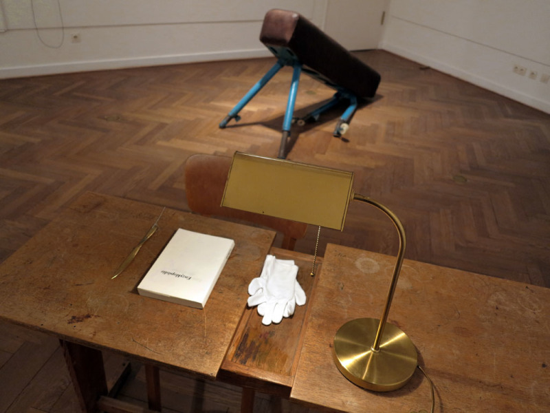 ein Schreibtisch mit einem Buch, weißen Handschuhen und Lampe aus der Vogelperspektive