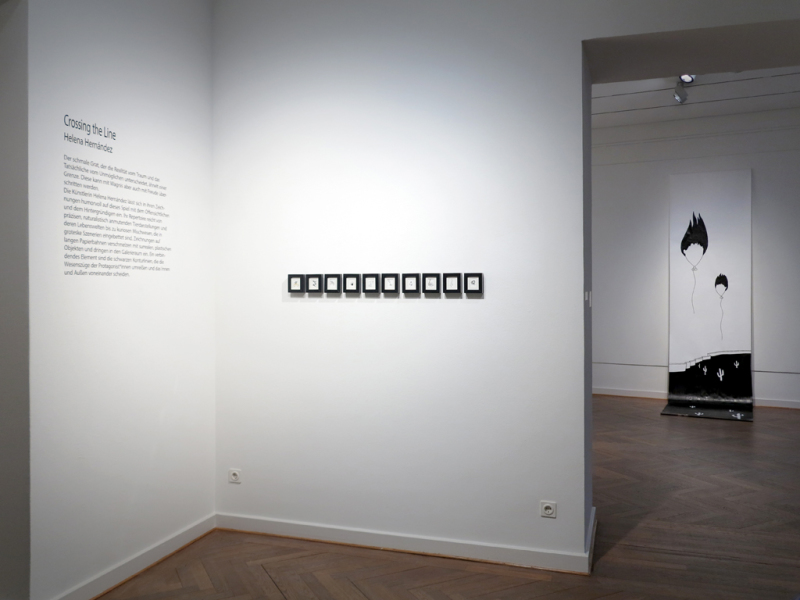 BU:Im vorderen Ausstellungsraum sind 10 kleinformatige, gerahmte Objekte zu sehen. Im hinteren Ausstellungsraum sind auf einer langen Papierbahn zwei ballonähnliche über eine Mauer hinwegfliegende Köpfe dargestellt.