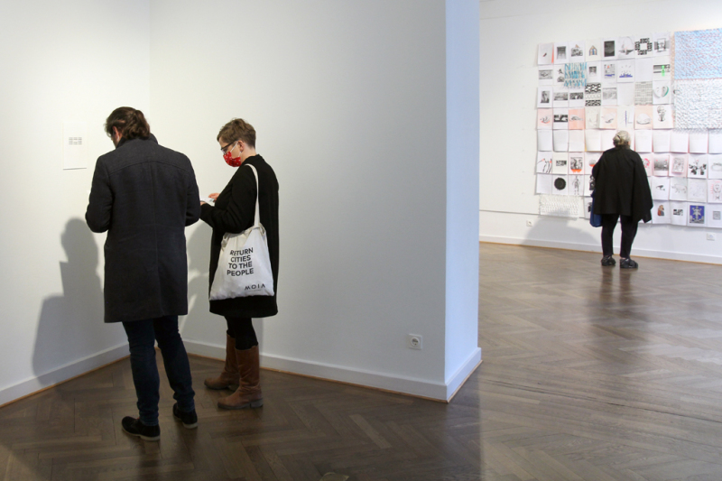 ein Pärchen steht vor dem Werk von Eugen Gomringer und eine Besucherin steht vor dem Werk von Ina Geißler