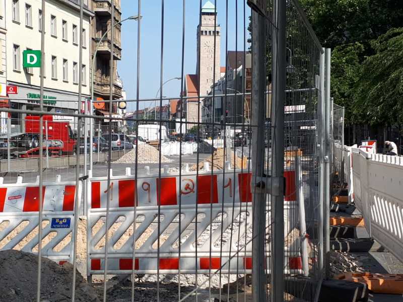 Foto einer Baustelle hinter einem Bauzaun, im Hintergrund ist das Rathaus Neukölln zu sehen
