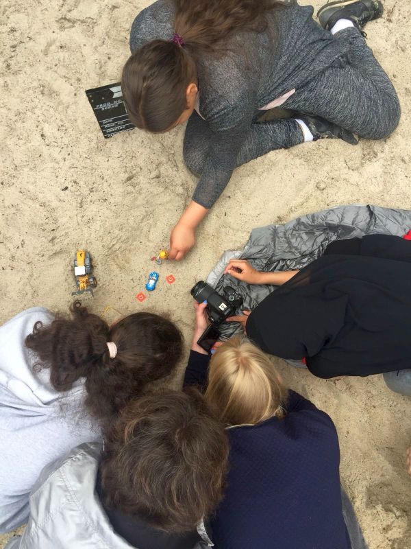 Blick von oben auf mehrere Mädchen und Frauen, die im Sand eine Spielzeugbaustelle filmen