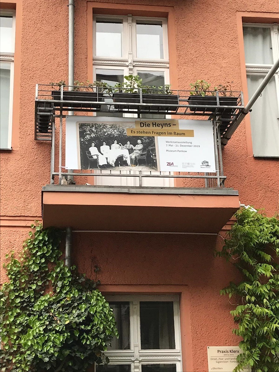 Balkon mit Werbeschild zur Ausstellung: "Die Heyns - es stehen Fragen im Raum."