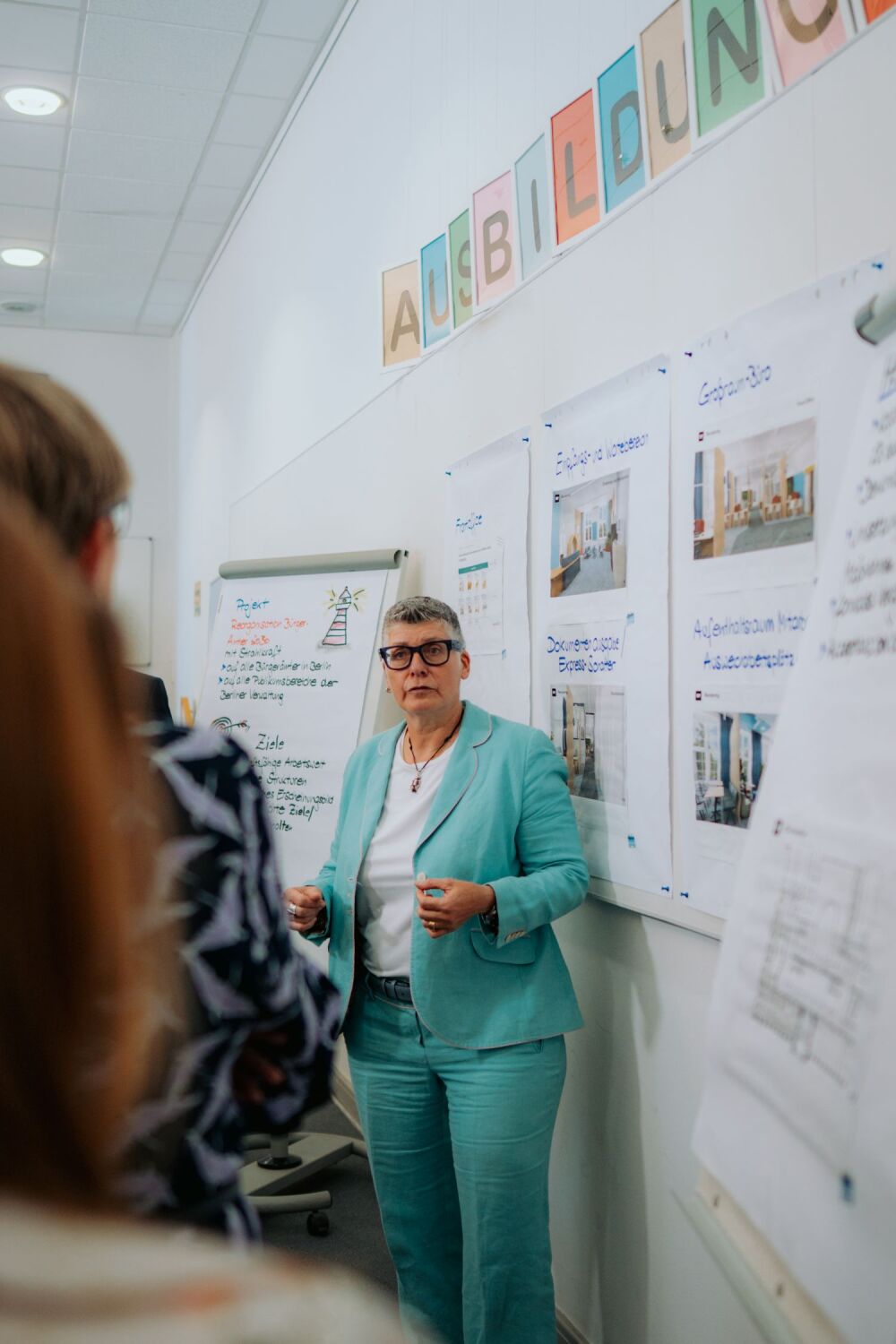Die Leiterin des Bürgeramts Schöneberg steht vor beschrifteten Flipchart-Blättern, die an einer Pinnwand angebracht sind.