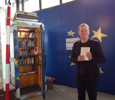 Senator Dr. Lederer mit Buch vor der BücherboXX Europa im Foyer der Brunnenstr. 188/190