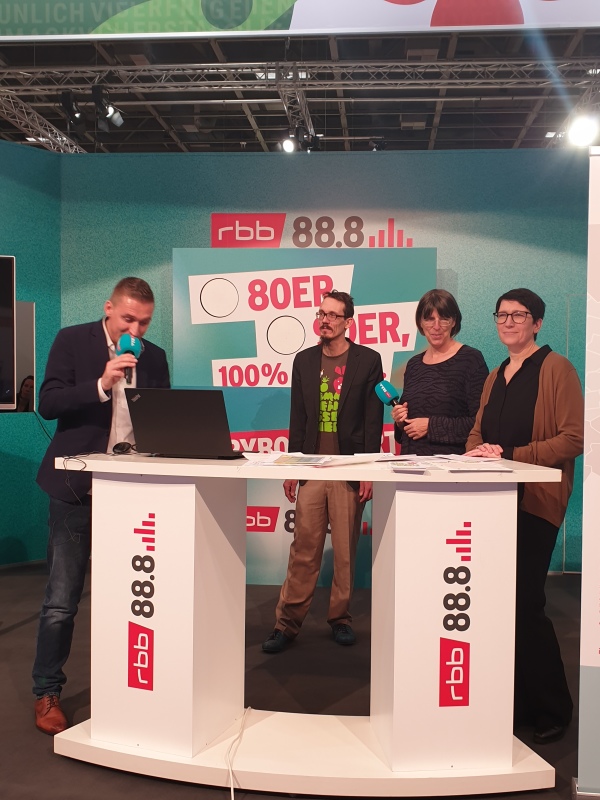 4 Personen stehen hinter einem Tresen auf der Radio 88.8 Bühne in der Berlin-Halle
