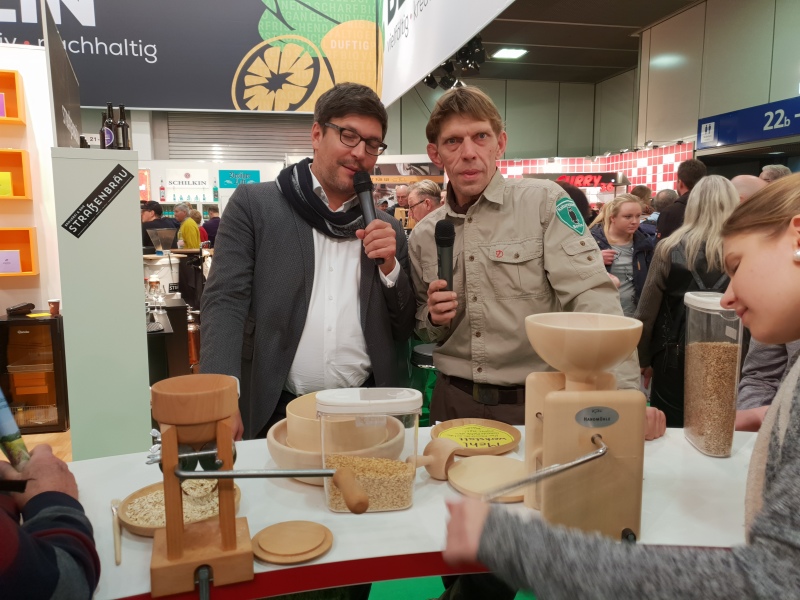 Senator Dr. Dirk Behrendt und Björn Lindner hinter einem Tisch mit Mehlmahlgeräten und einem Gerät zur Herstellung von Haferflocken
