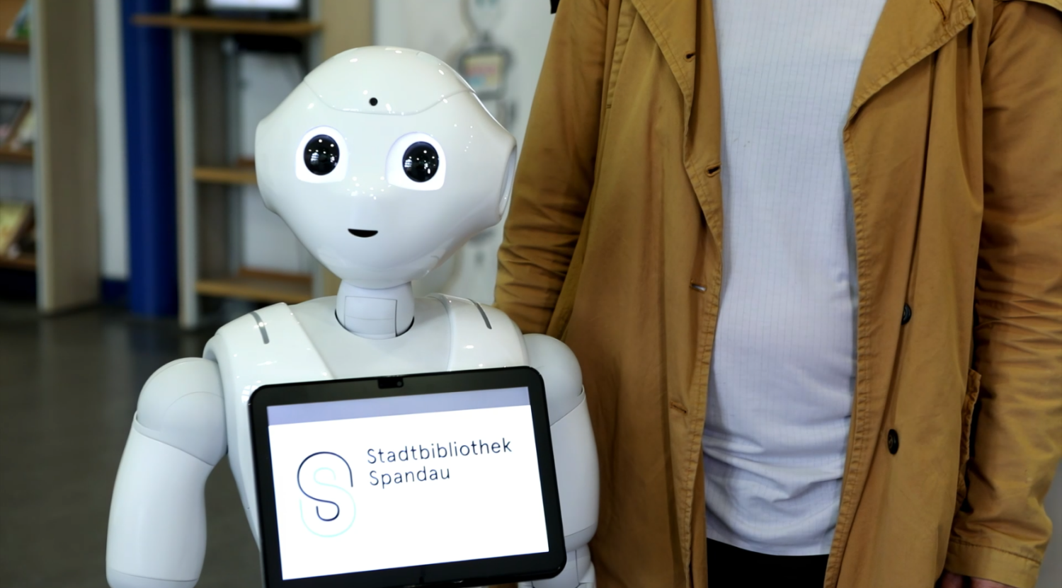 Ein Roboter mit einem Tablet auf der Brust mit der Aufschrift "Stadtbibliothek Spandau"