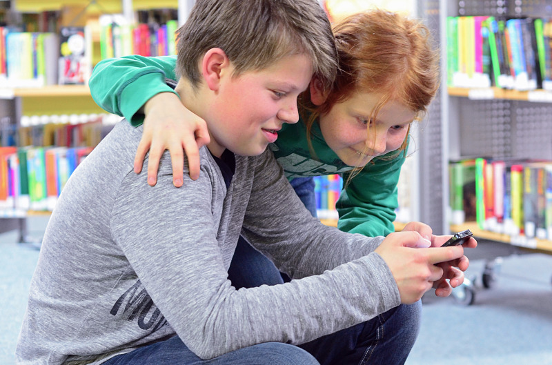 Bruder und Schwester nutzen in der Bibliothek ihr Smartphone mit HotsPlots