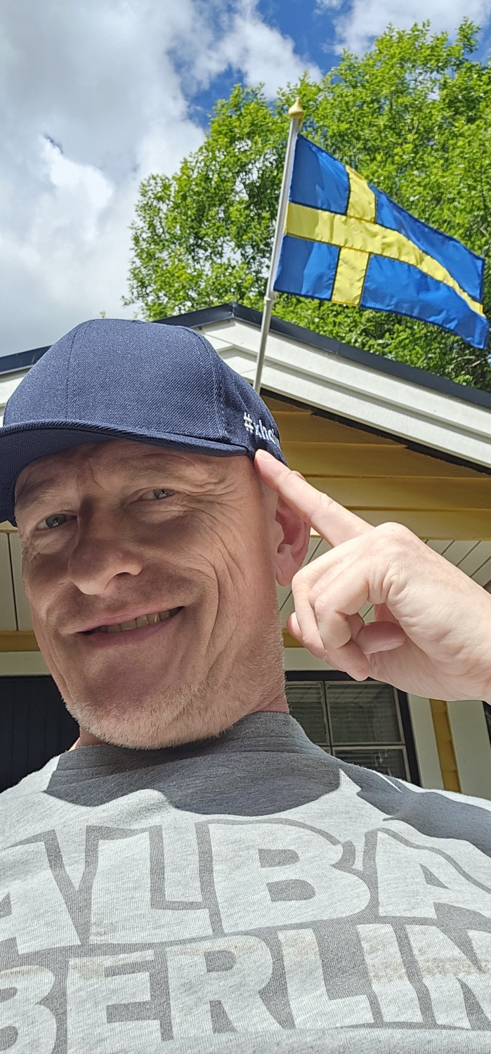Person mit Basecap vor einem Haus an dem die Schwedenflagge weht
