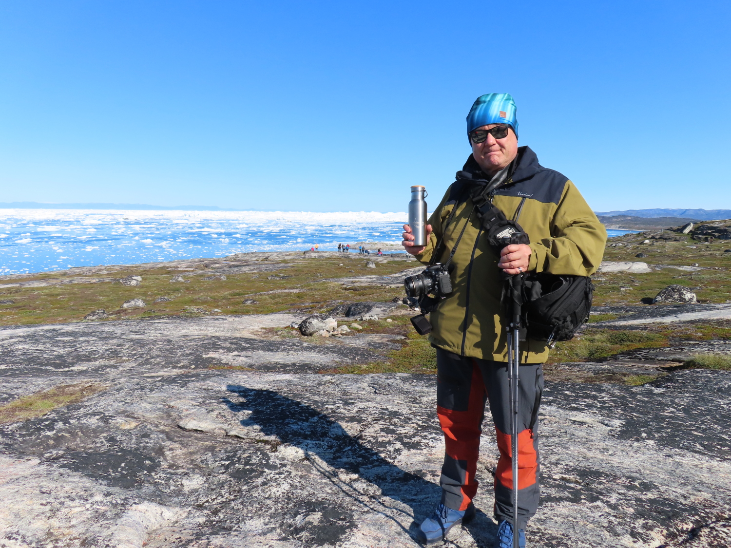 Person mit Wanderstöcken in der grönländischen Natur mit gravierter Edelstahlflasche in der Hand