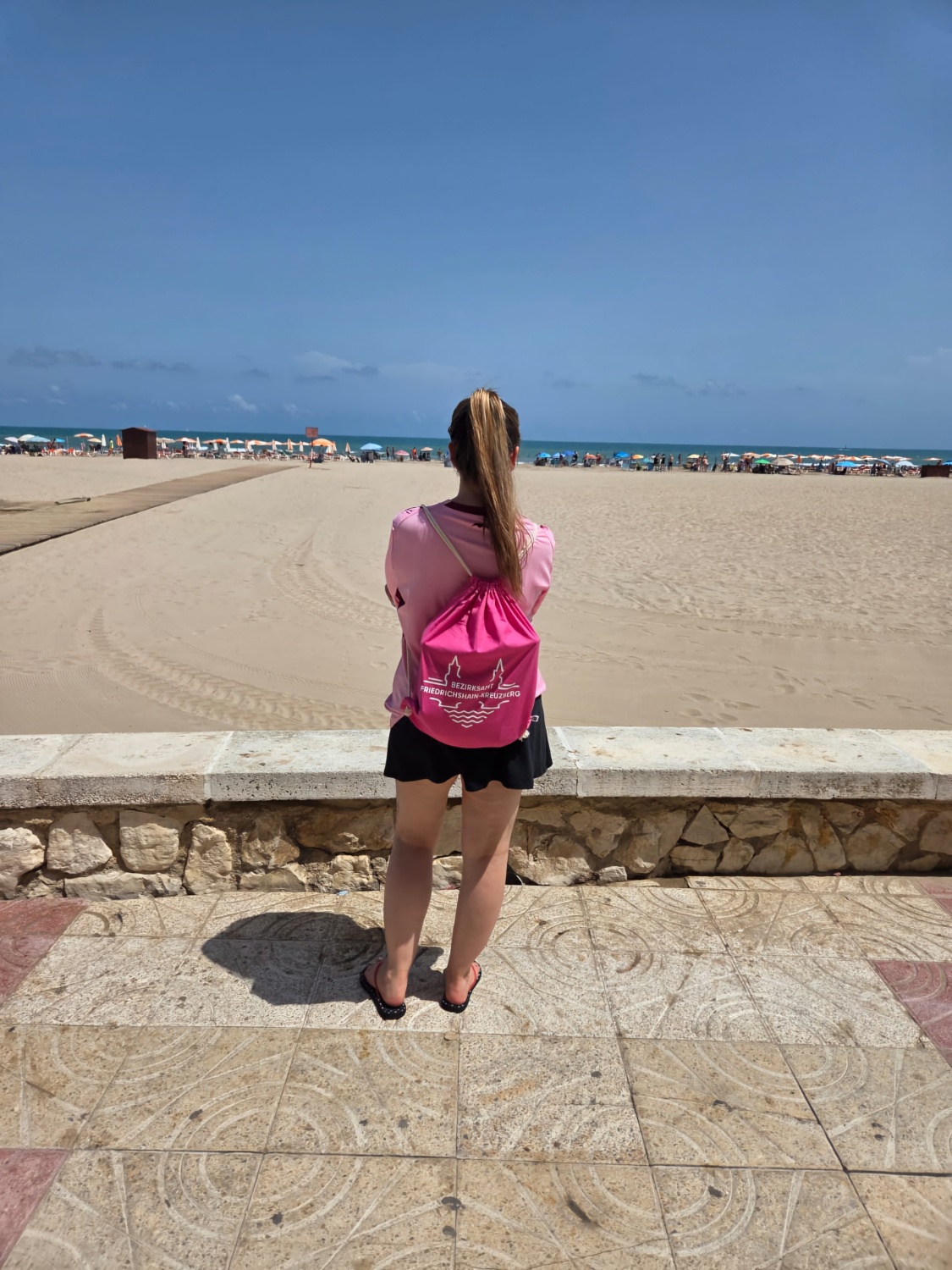 Person mit langem Zopf und Turnbeutel vor Strandpanorama