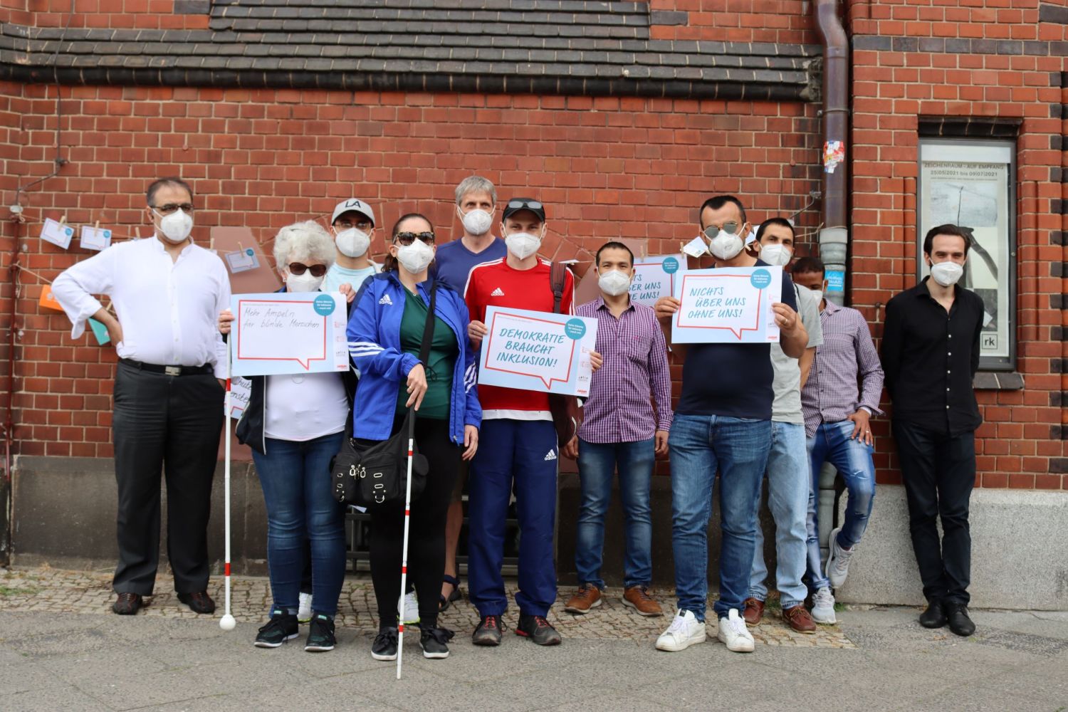 Teilnehmer:innen des SEHZENTRUM Berlin haben den Aktionstag besucht. Auch sie haben Forderungen: "Mehr Ampeln für blinde Menschen", "Demokratie braucht Inklusion", "Nichts über ohne uns". Zwei Teilnehmerinnen haben Blindenleitstöcke.