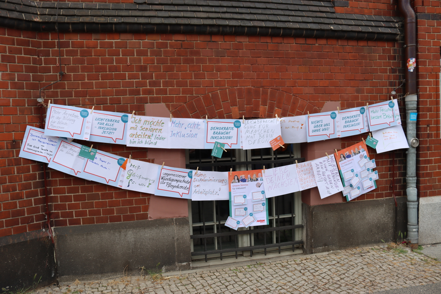 Zwei Wäscheleinen mit unterschiedlichen Forderungen und Wünschen. Auf den Plakaten steht beispielsweise: "Mehr Angebote in der Bildung für blinde Menschen", "Ich möchte mit Senioren arbeiten, aber ich bin blind.", "mehr echte Inklusion", "angemessener Kündigungsschutz für Pflegedienste" und "mehr Respekt für behinderte Menschen".