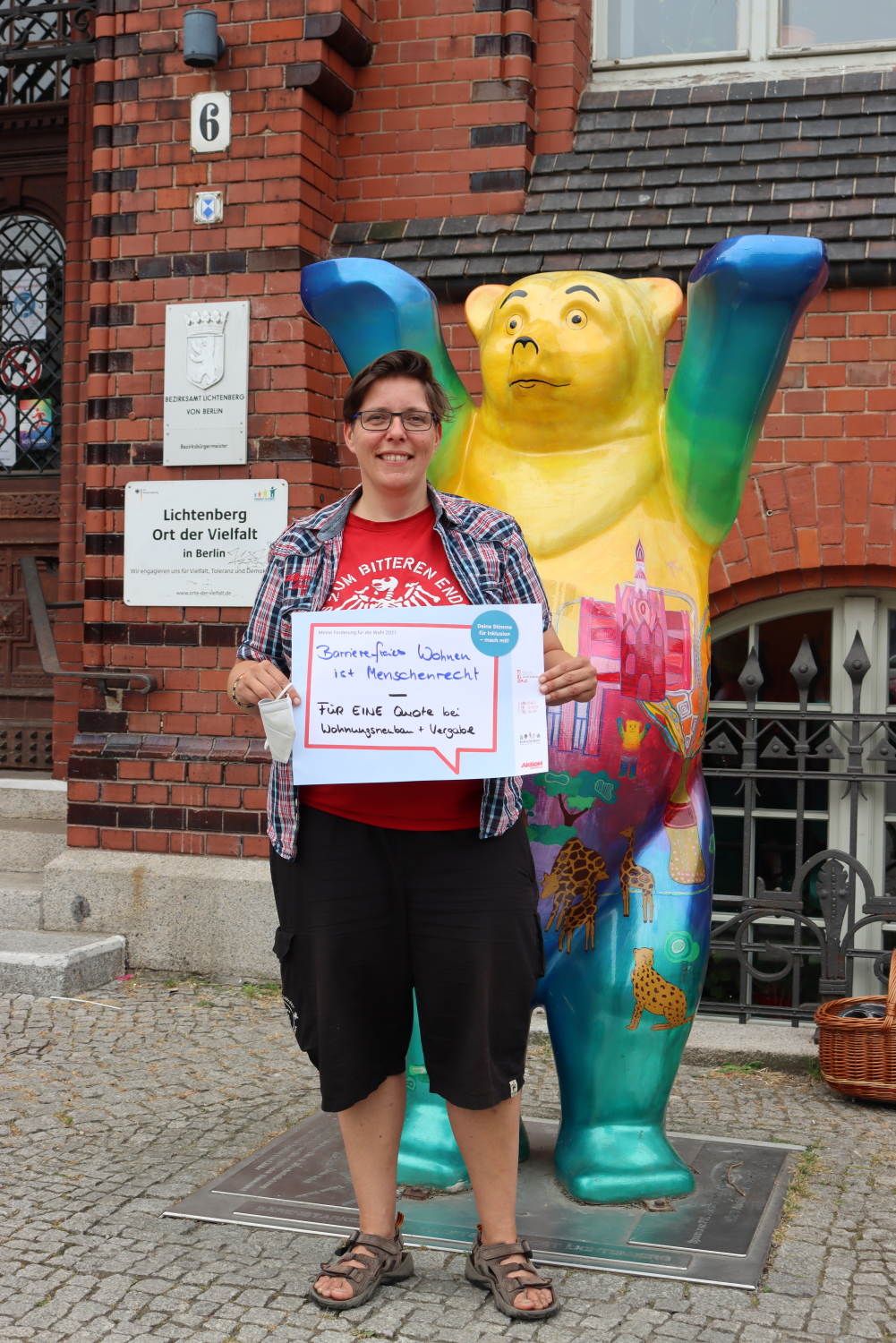 Die BVV-Verordnete der Partei DIE LINKE, Claudia Engelmann, fordert: "Barrierefreies Wohnen ist Menschenrecht - FÜR EINE Quote bei Wohnungsneubau + Vergabe". Hinter ihr steht ein Buddy-Bär.
