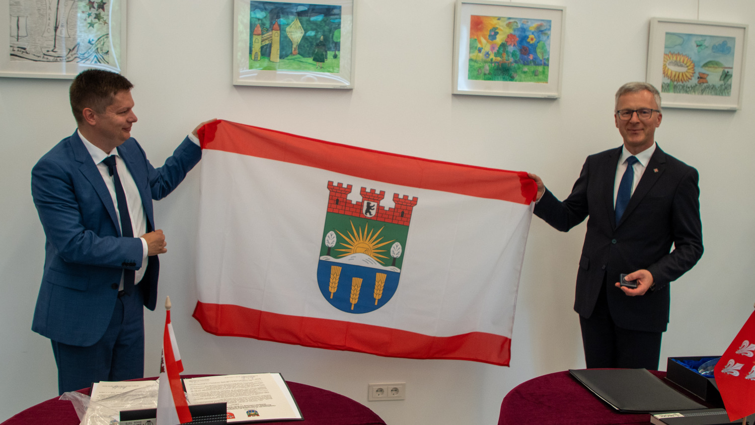 Bezirksbürgermeister Martin Schaefer und der Bürgermeister der Stadt Jurbarkas, Skirmantas Mockevičius, halten eine Fahne mit dem Wappen von Lichtenberg hoch.