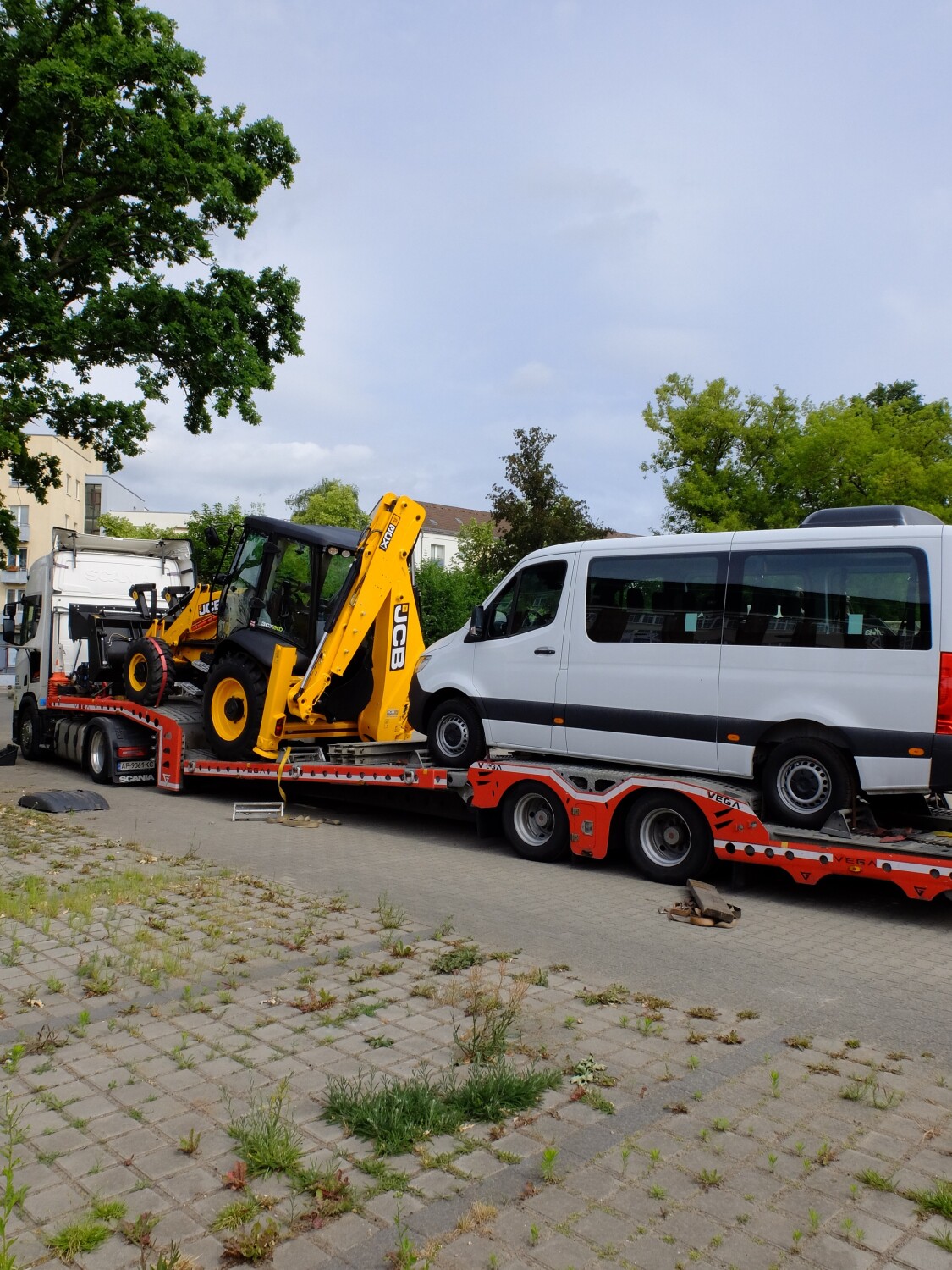 ein Sprinter Kastenwagen mit Rollrampe und ein Multifunktionsradlader stehen auf einem Auflieger von einem LKW